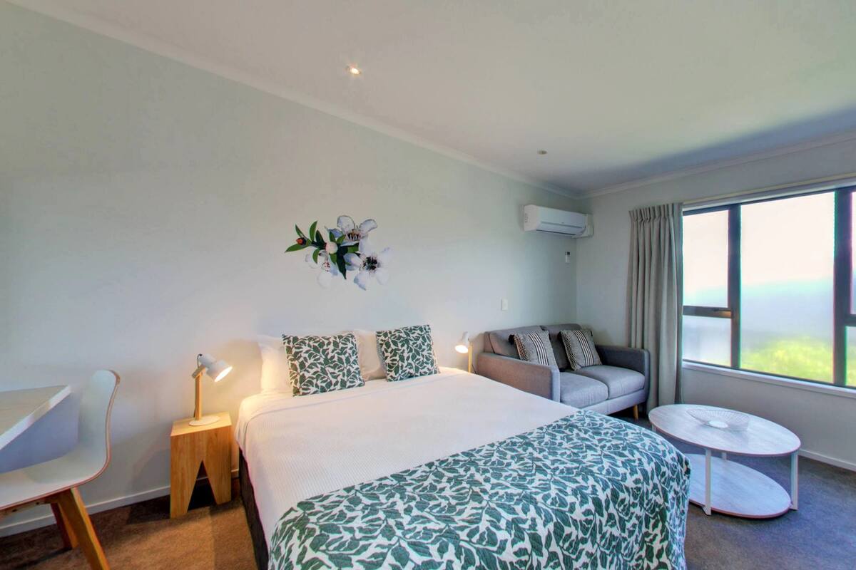 Habitación de hotel con cama, sofá, una mesita, escritorio y ventana con cortinas.