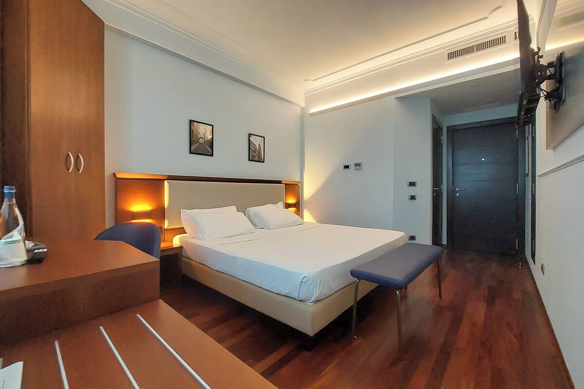 Ein Hotelzimmer mit einem Bett, einem Nachttisch, einer Bank und einem Schreibtisch mit Stuhl.