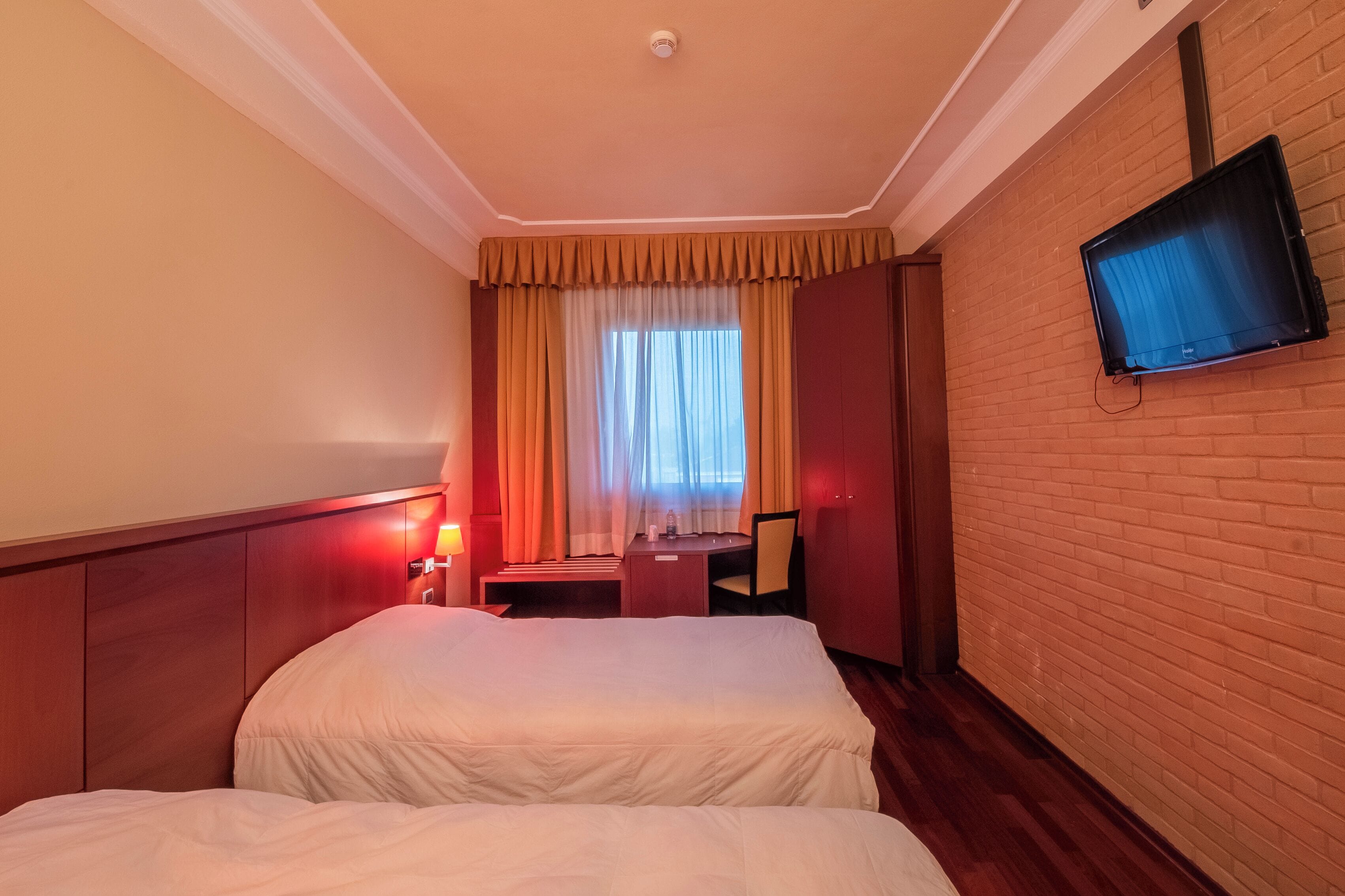 Habitación de hotel con dos camas, un escritorio, una silla, un televisor montado en la pared y una ventana con cortinas.