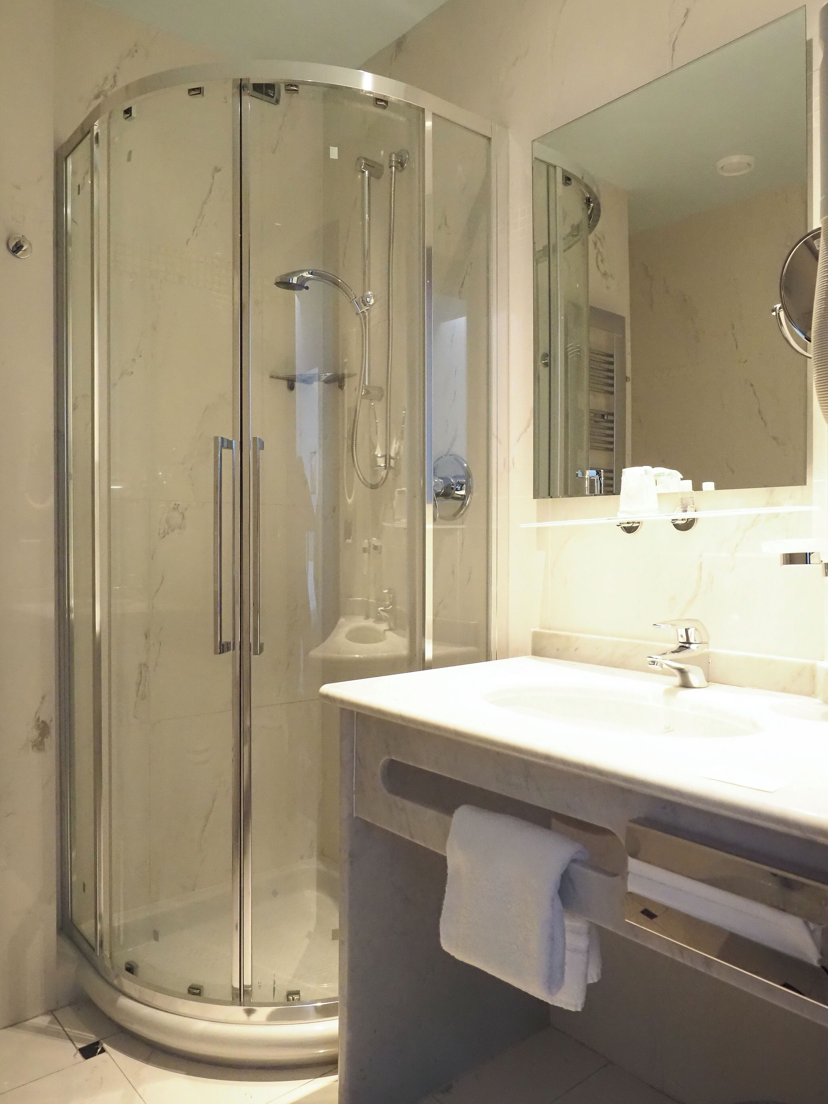Un baño moderno con cabina de ducha acristalada, un lavabo con espejo y un perchero para toallas.