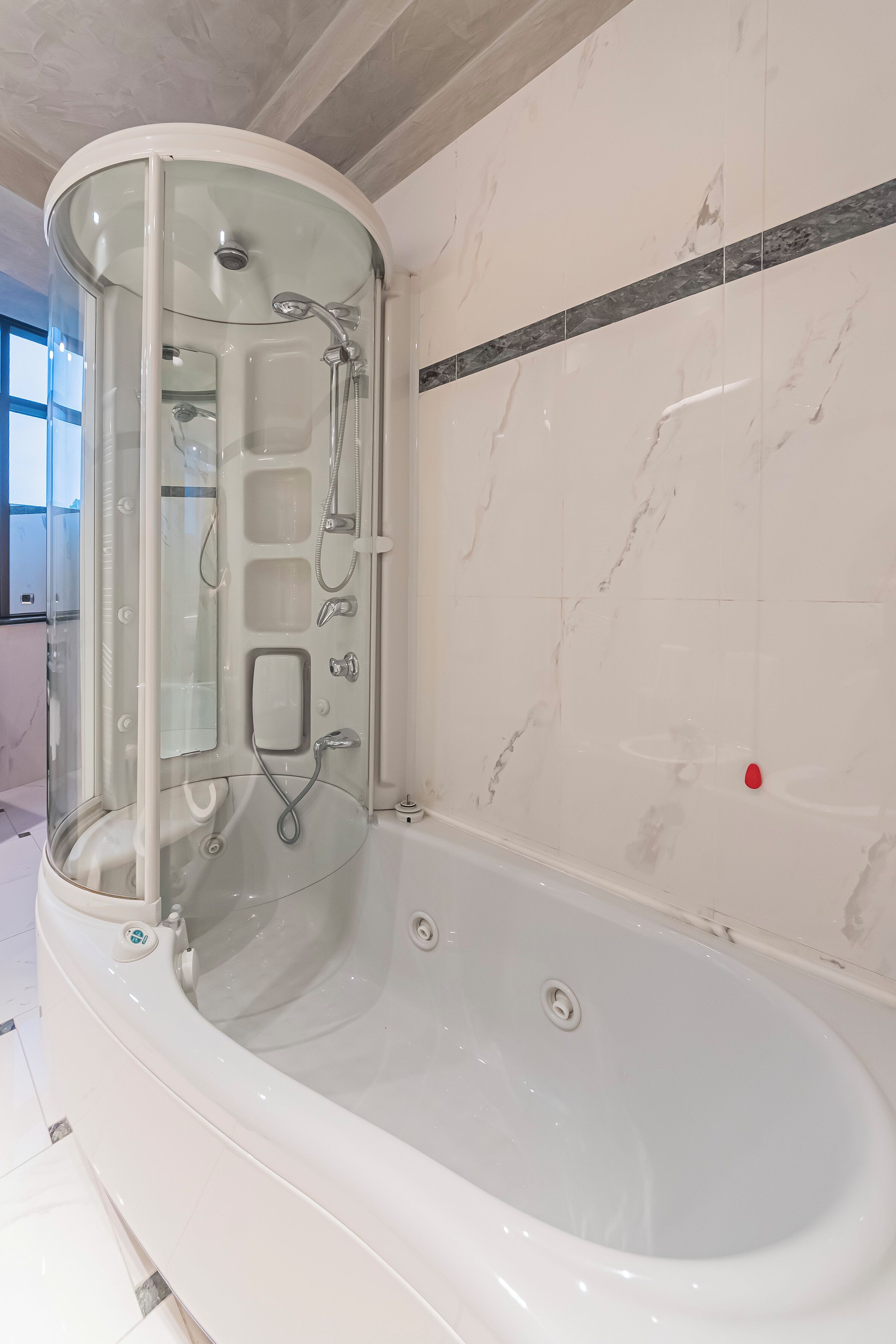 Une salle de bain moderne dotée d’une douche à parois de verre, d’une baignoire sur pieds et de murs recouverts de carreaux de marbre.