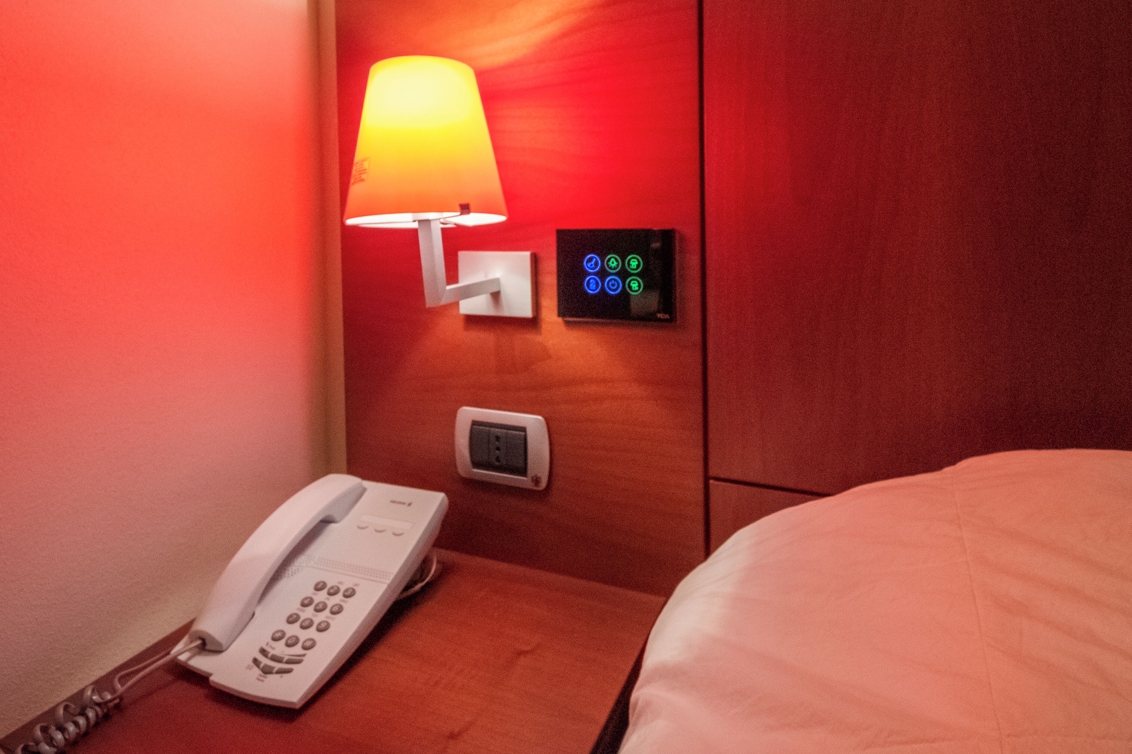 Habitació d'hotel amb una làmpada de nit, un panell de control, un telèfon i un llit.