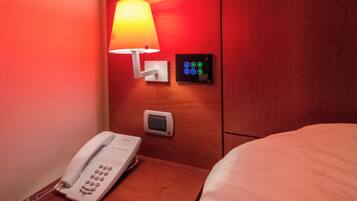 A hotel room with a bedside lamp, a control panel, a phone, and a bed.