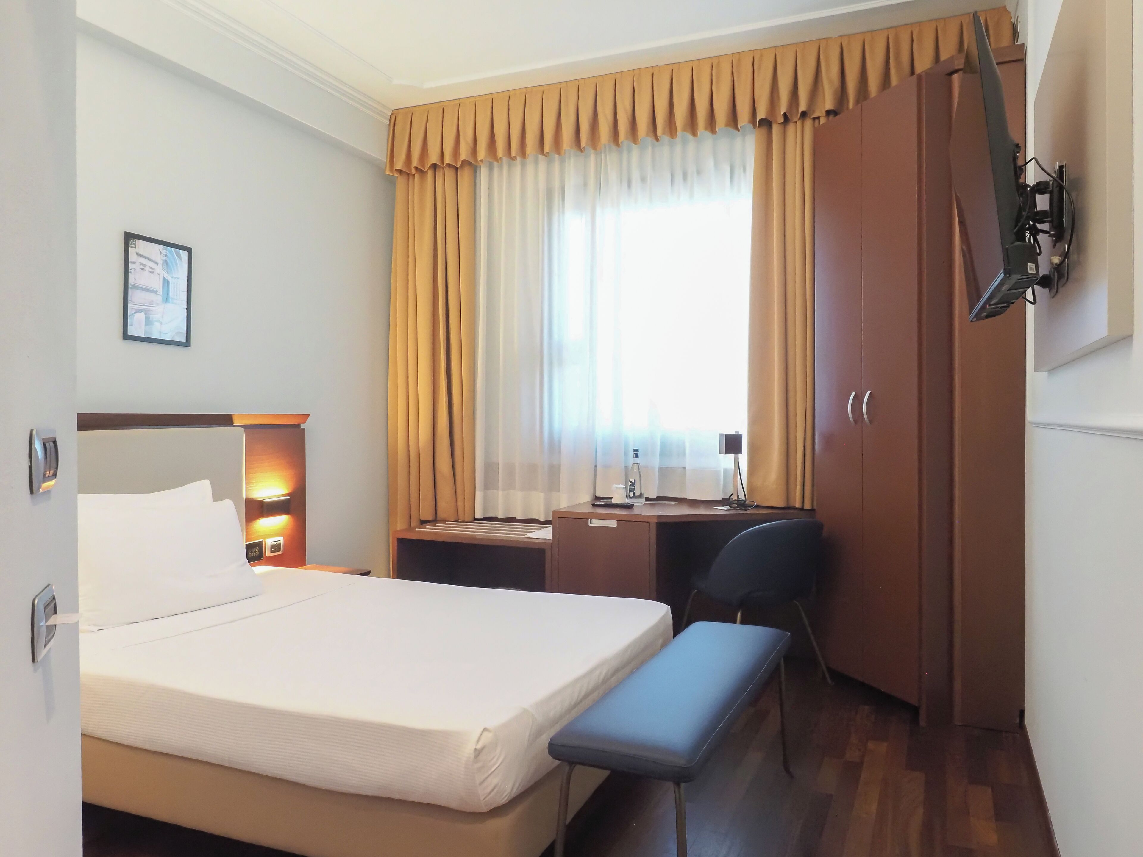 A hotel room with a bed, desk, chair, and a television mounted on the wall.