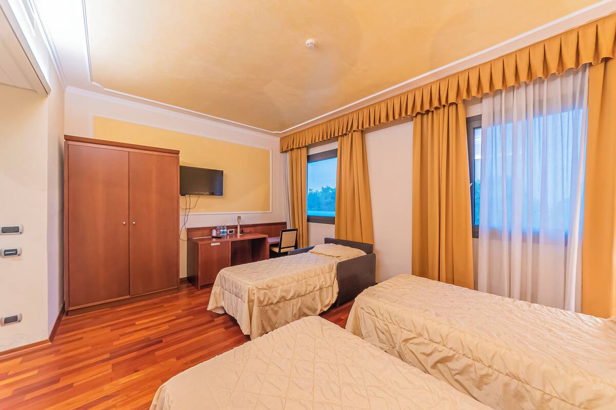 Ein Hotelzimmer mit zwei Betten, einem Schreibtisch, einem Kleiderschrank und einem Fernseher.
