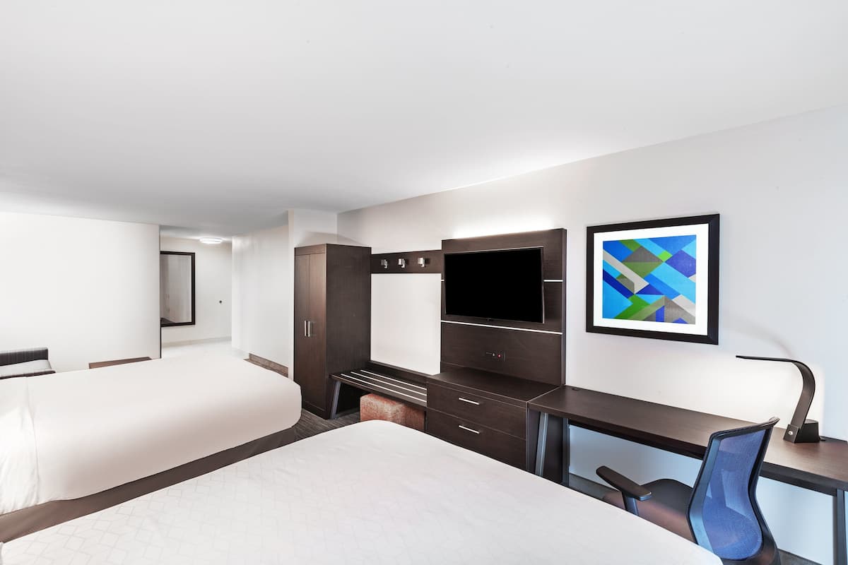 A modern hotel room with a large bed, a desk with a chair, a flat-screen TV, and a framed abstract painting on the wall.