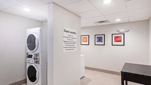 Uma área de lavanderia para hóspedes, com uma placa, uma máquina de lavar e três obras de arte emolduradas na parede.