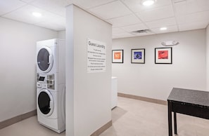 A guest laundry area with a sign, a washing machine, and three framed artworks on the wall.
