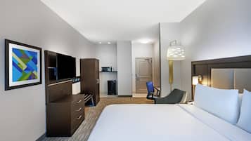 Ett hotellrum med en säng, ett skrivbord, en stol, en tv, en minibar och en dörr.