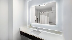 Um banheiro moderno com toucador branco, espelho e chuveiro visível no reflexo.
