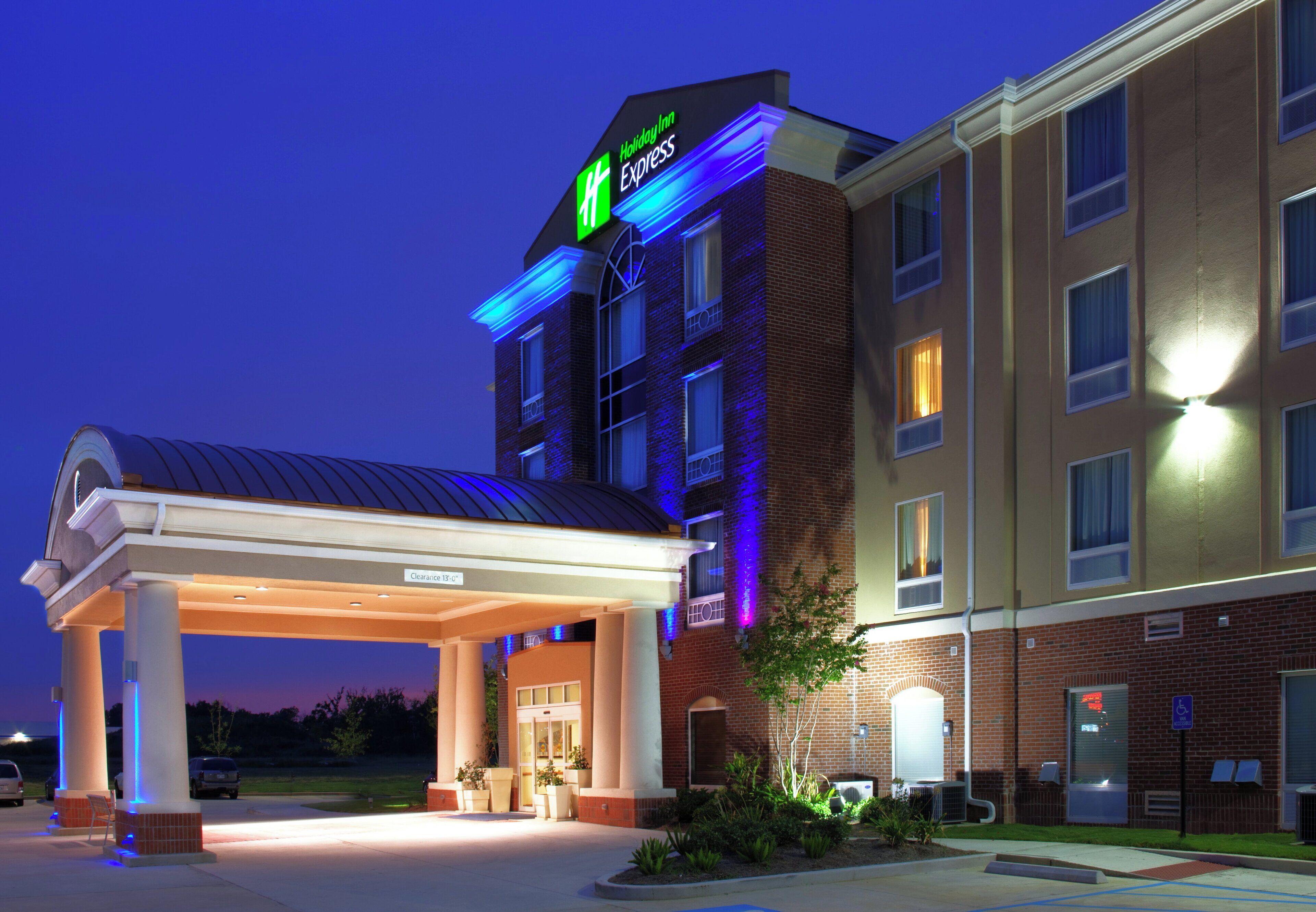 Un hotel Holiday Inn Express con entrada cubierta, fachada de ladrillo y señalización iluminada.