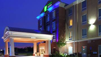 Un hotel Holiday Inn Express con entrada cubierta, fachada de ladrillo y señalización iluminada.