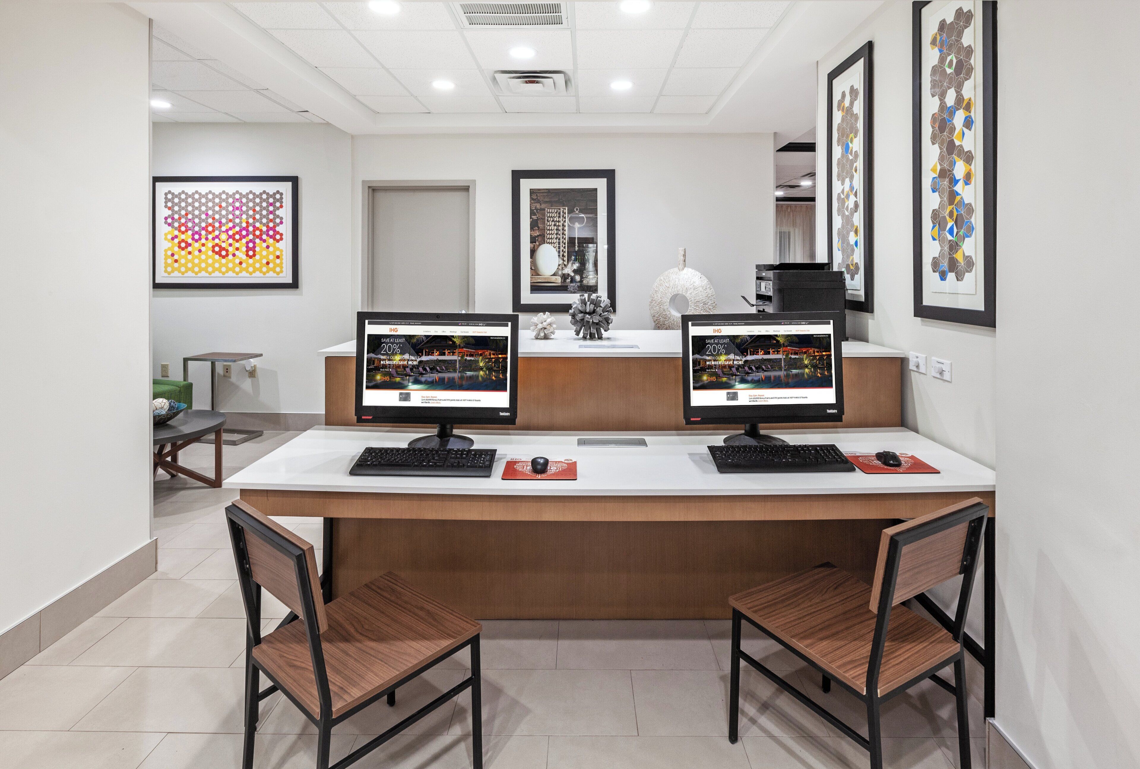A reception desk with two monitors, a decorative vase, and framed artwork on the wall.