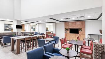 A modern dining area with multiple seating options including booths and tables, a flat-screen TV mounted on the wall, and a wooden accent wall.