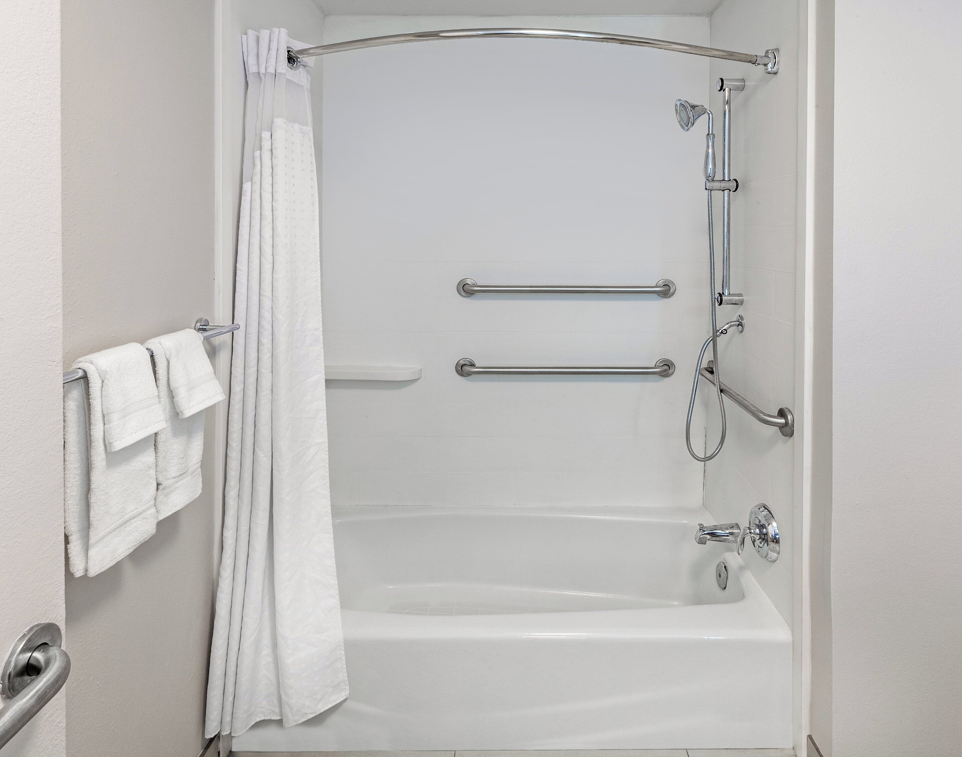 A modern bathroom with a bathtub, shower, and grab bars.