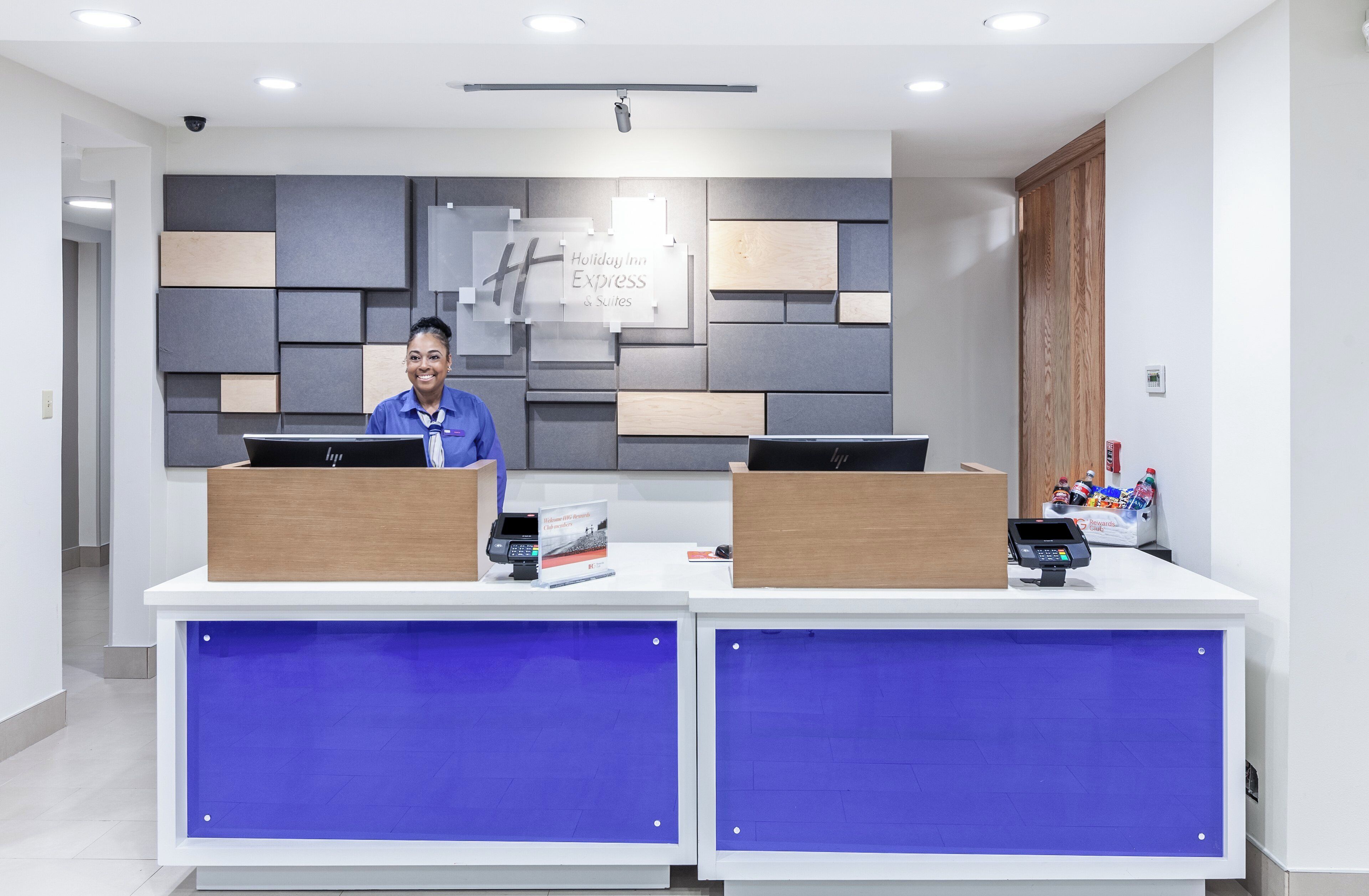 Una reception dal design moderno, una segnaletica con la scritta 'Holiday Inn Express & Suites' e una telecamera di sicurezza sopra.