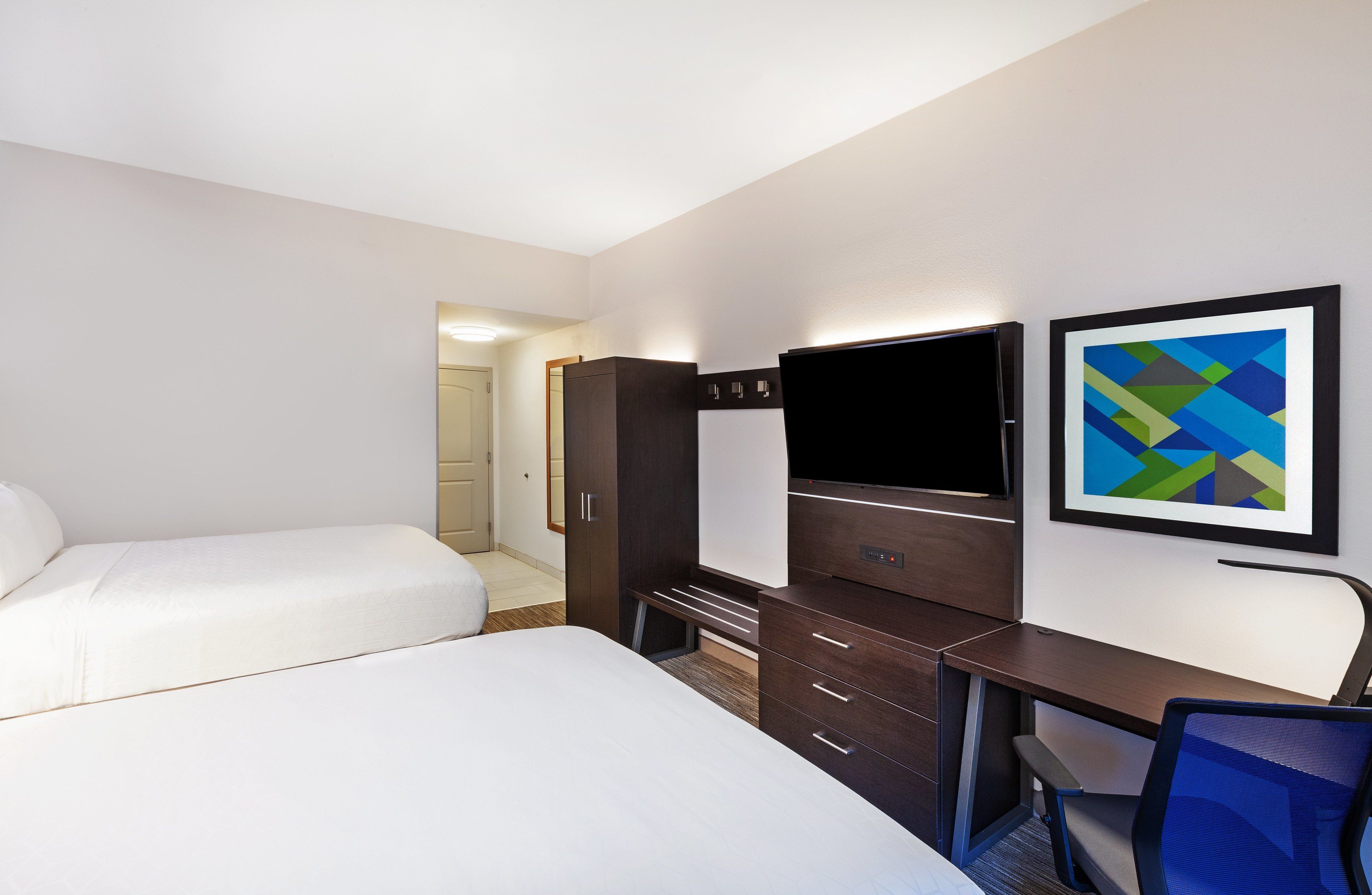 Habitación de hotel con dos camas, un escritorio con silla, televisor y un cuadro abstracto enmarco.