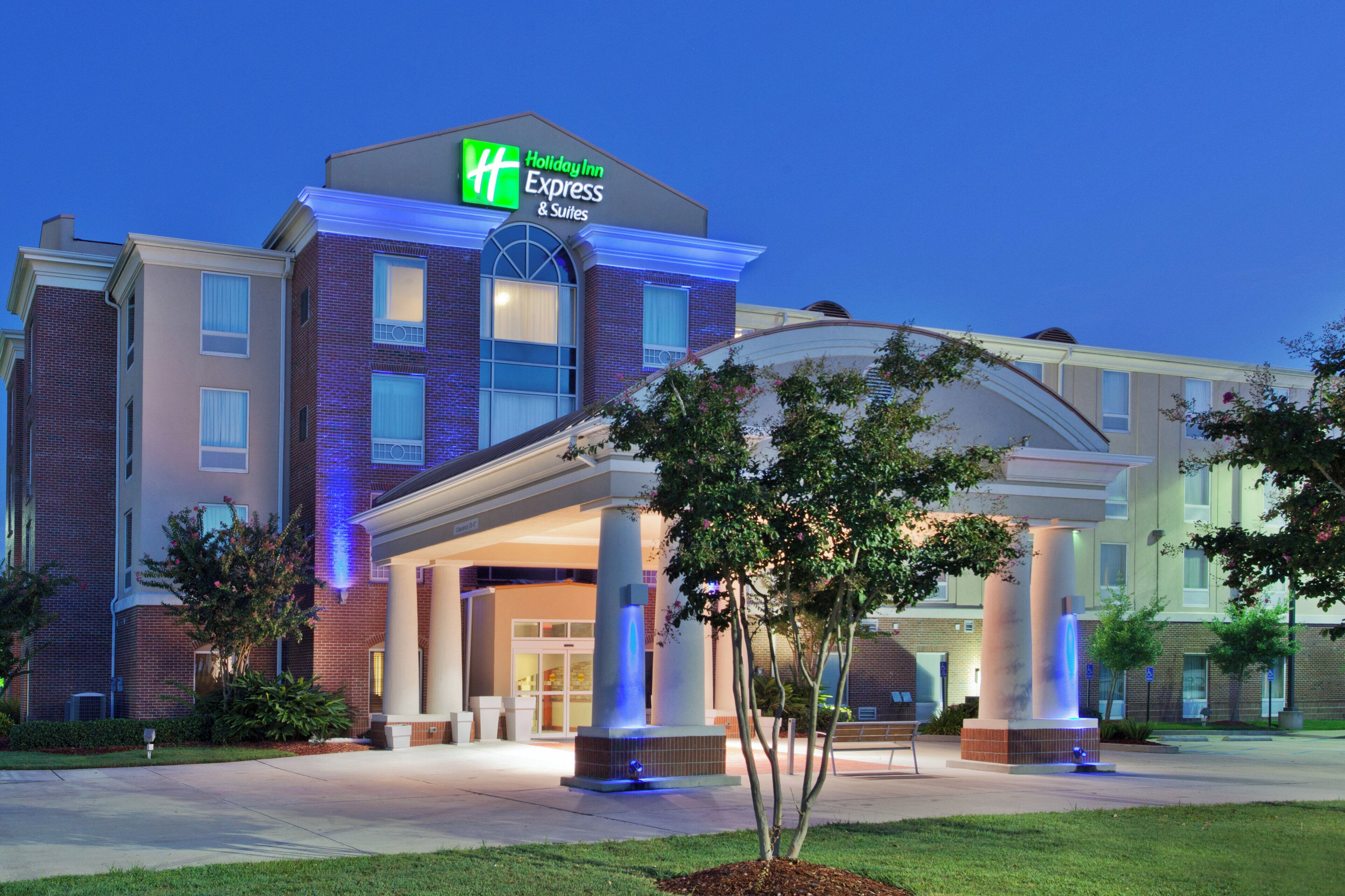 A Holiday Inn Express & Suites hotel with a brick facade, large windows, and a covered entrance with columns.