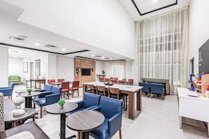 A modern hotel lobby with a dining area, seating arrangements, and a large window.