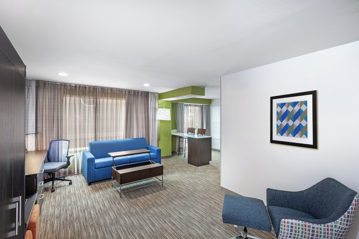 Quarto de hotel com um sofá azul, uma escrivaninha, uma cadeira e uma mesinha.