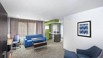 A hotel room with a blue sofa, a desk, a chair, and a small table.