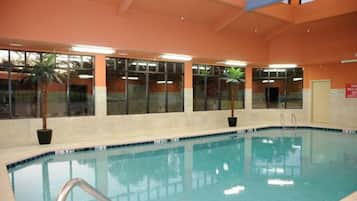 Piscina interior com água cristalina, rodeada por janelas e plantas em vasos.