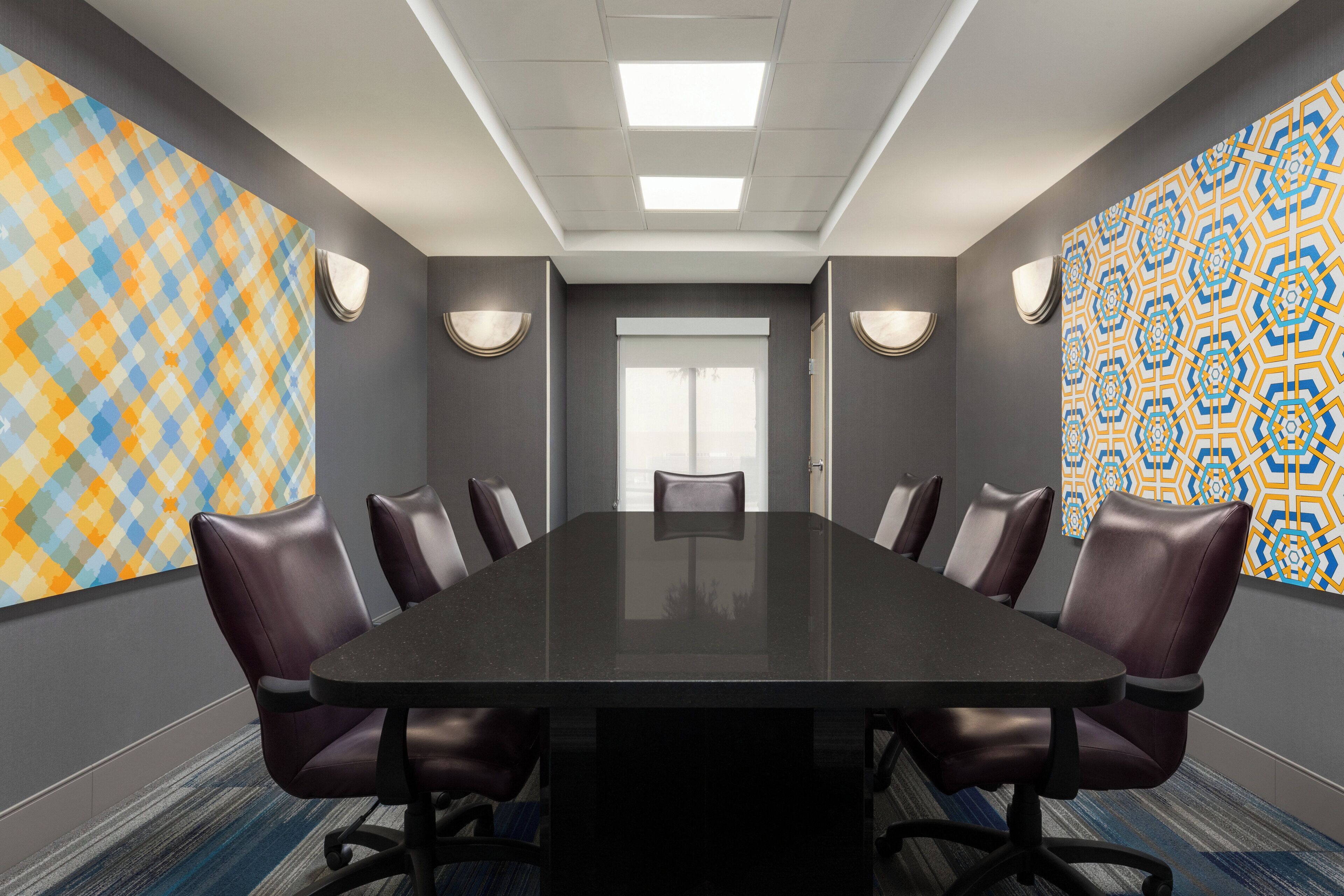 A conference room with a long table and leather chairs, two patterned walls, and ceiling lights.