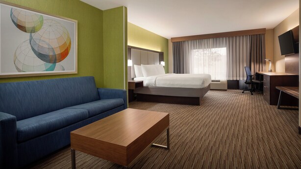 Una habitación de hotel con una cama, un sofá azul, una mesa de centro de madera, un escritorio con una silla y un televisor en la pared.
