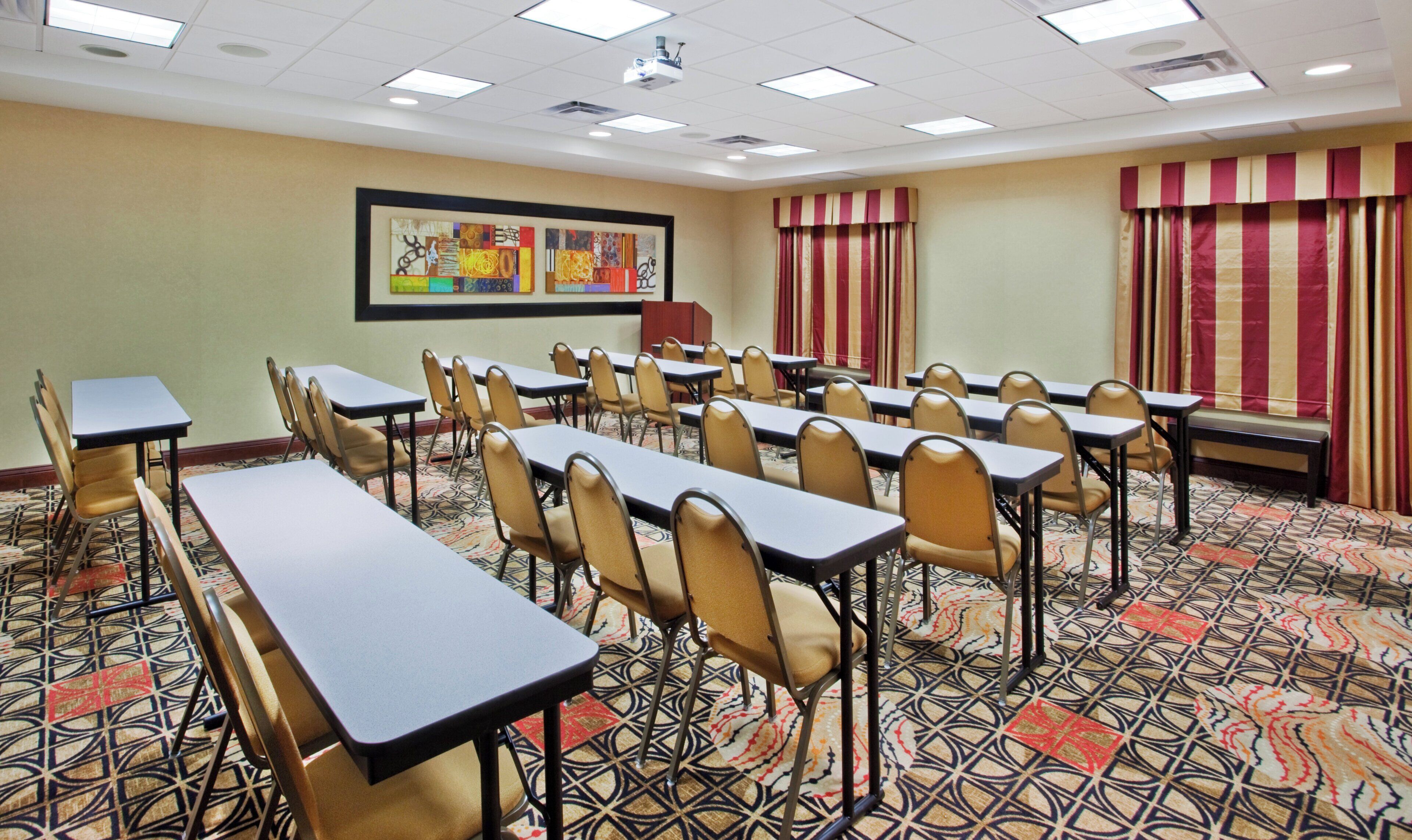 A conference room with tables and chairs, a projector, and a patterned carpet.