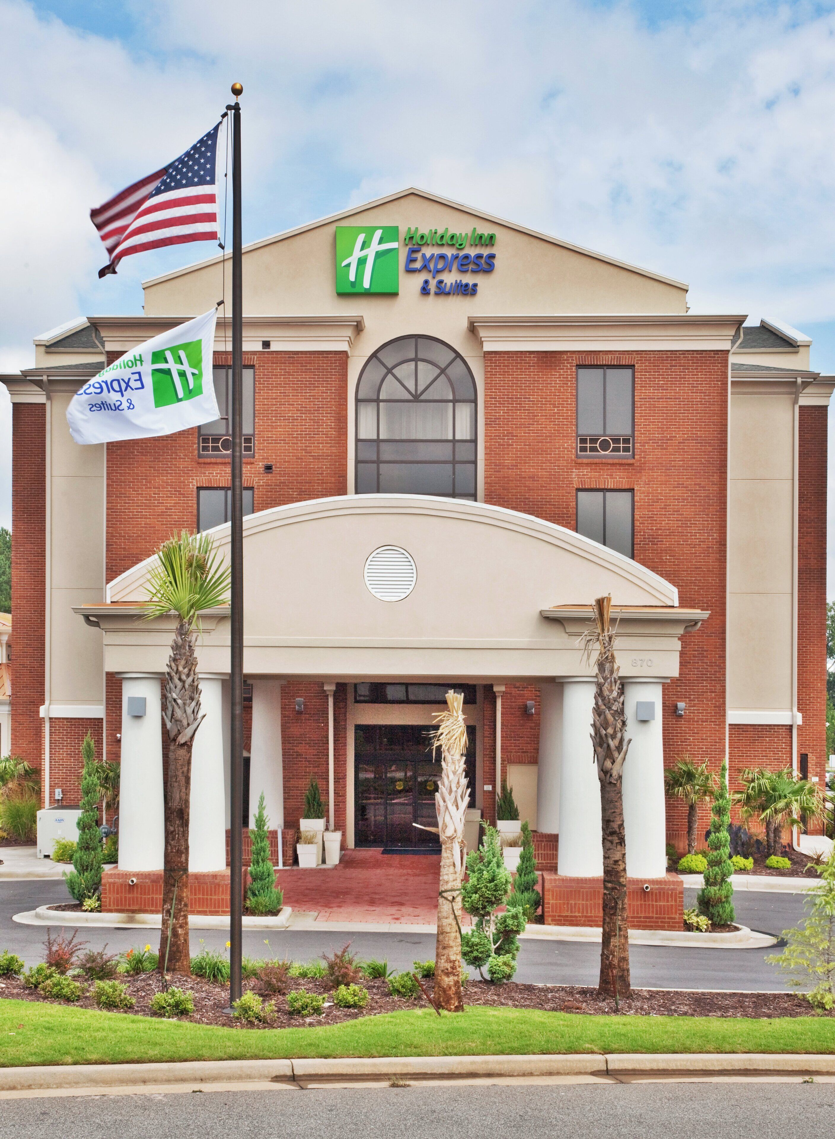 A Holiday Inn Express & Suites building with a brick facade, a central entrance with a canopy, and a flagpole with the American flag.