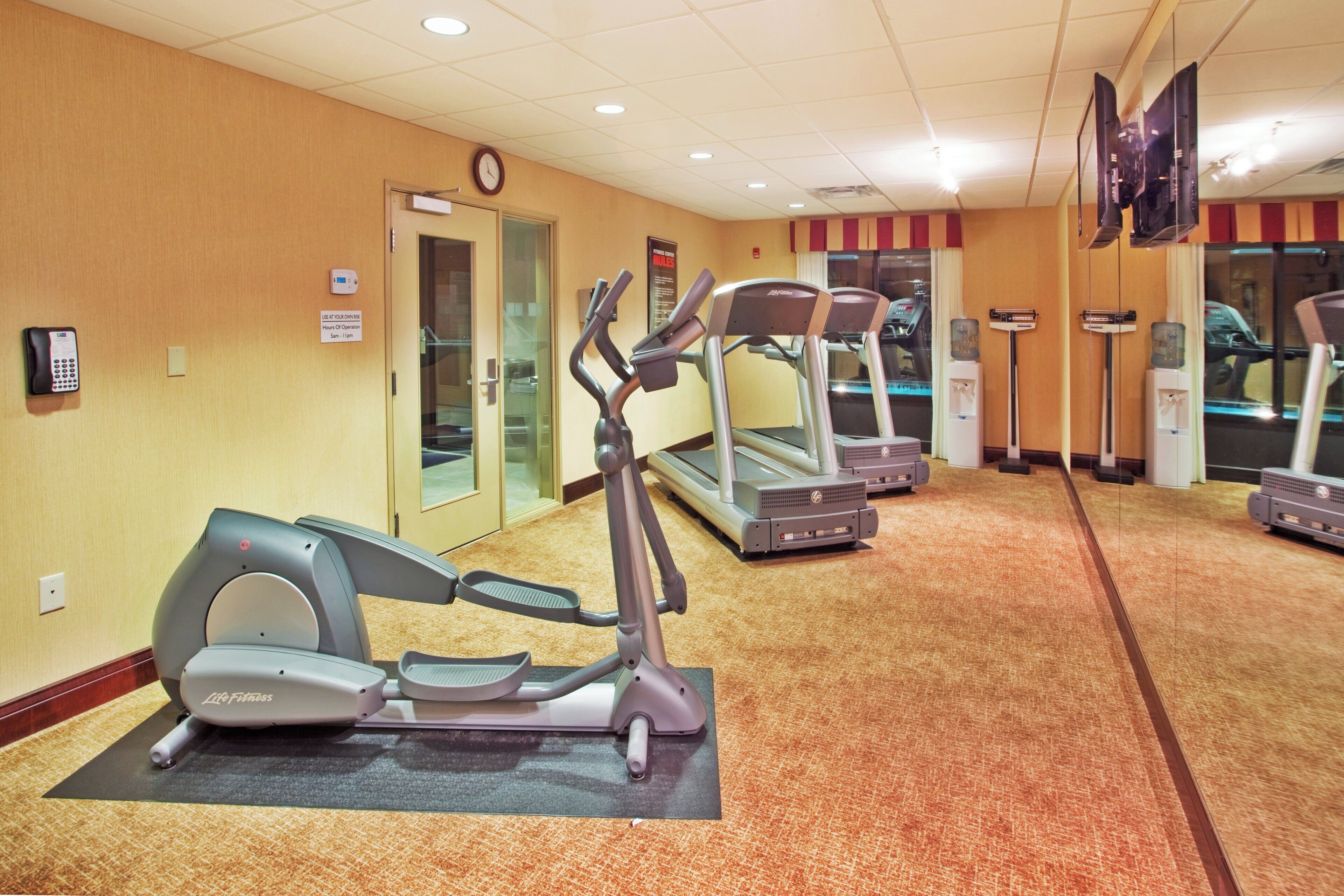 Ein Fitnessraum eines Hotels mit Laufbändern, einer Uhr und einem Wasserspender.