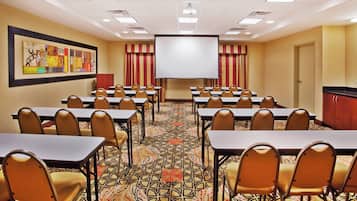 A conference room with tables and chairs, a projector screen, and a patterned carpet.