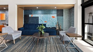 Un salon moderne comprenant un canapé bleu, deux fauteuils, une table basse et une plante décorative.