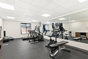 A gym with exercise equipment, a bench, a mirrored wall, and a window. - Holiday Inn Express & Suites Perry by IHG (Perry)