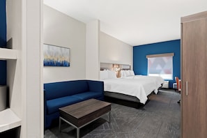A modern hotel room with a blue accent wall, a white bed, a blue sofa, and a wooden coffee table. - Holiday Inn Express & Suites Perry by IHG (Perry)