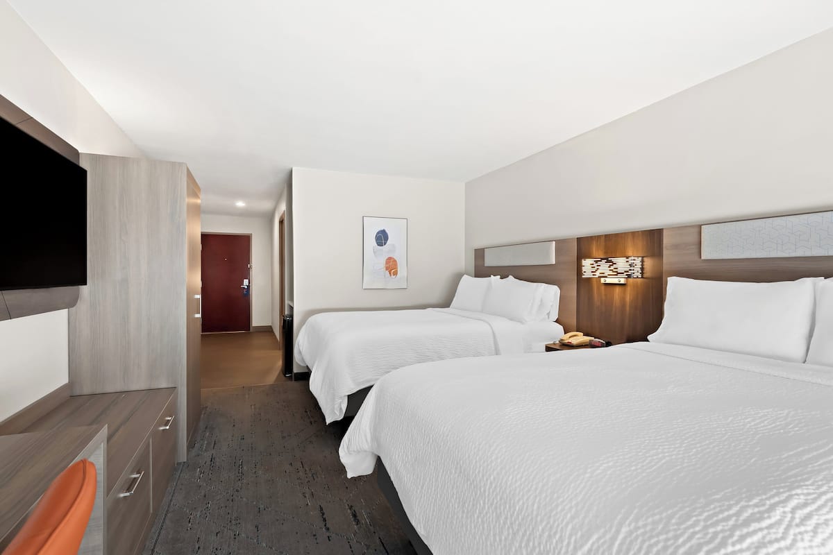 A hotel room with two beds, a desk, a TV, and a door leading to another room.