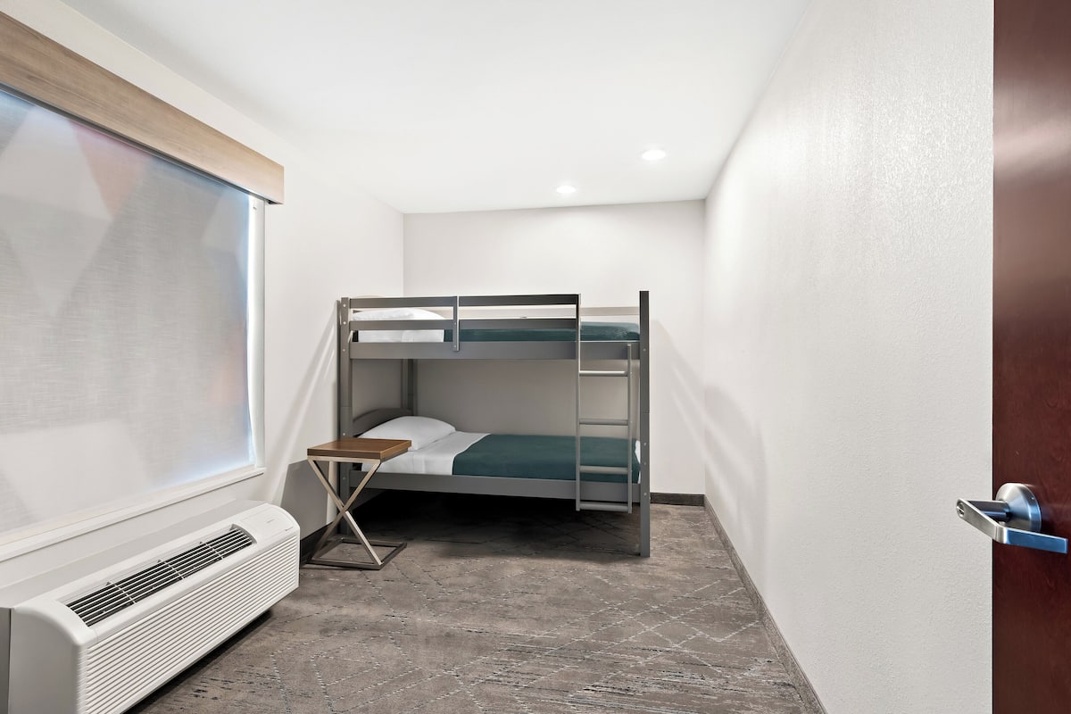 A small, modern room with a bunk bed, a heater, a small table, and a window.