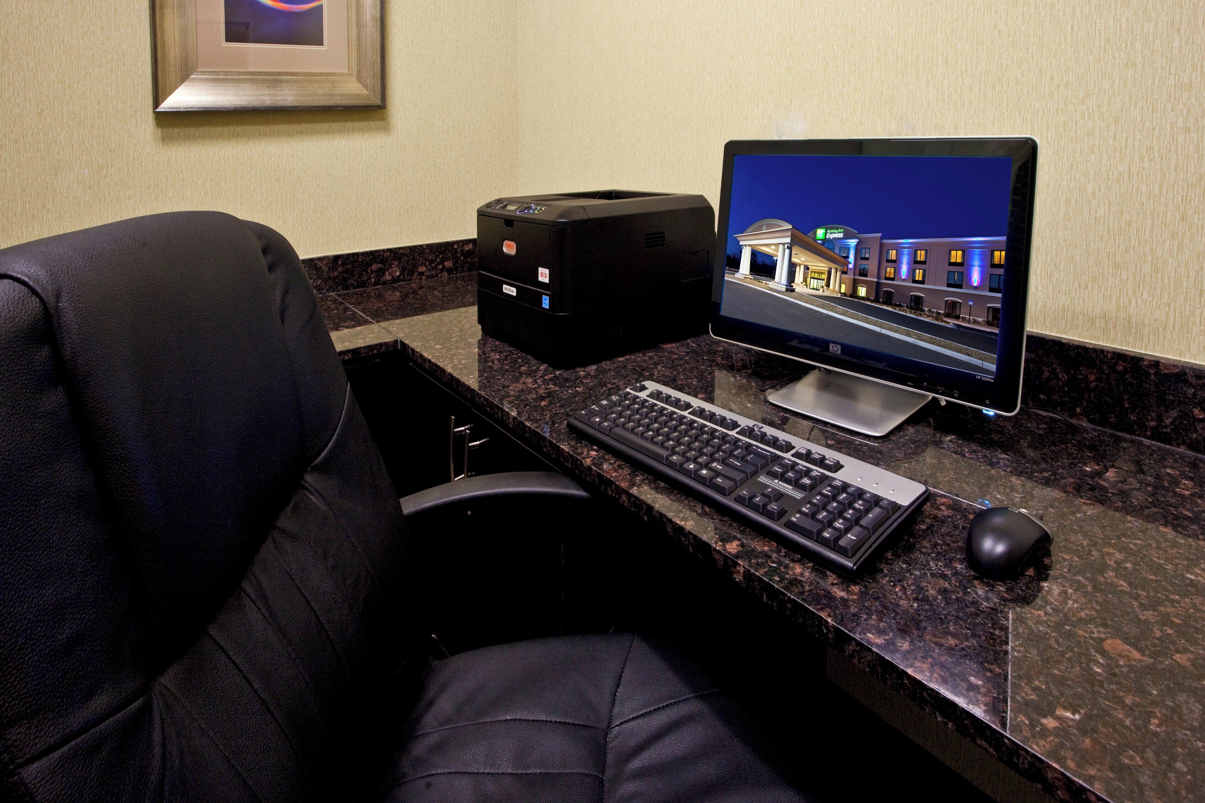 A hotel room with a desktop computer, a printer, a keyboard, a mouse, and a chair.