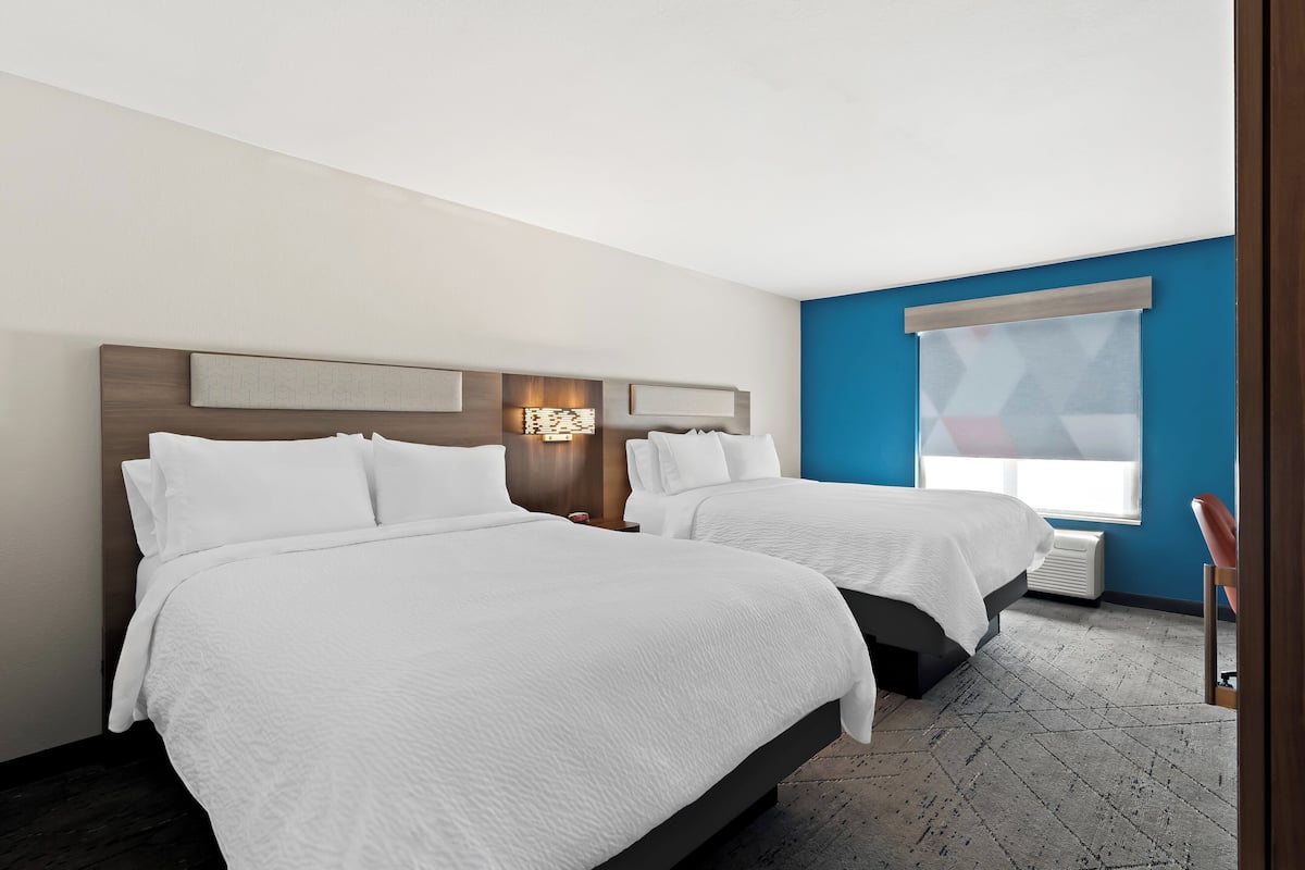 A hotel room with two beds, a large window, and a modern design.