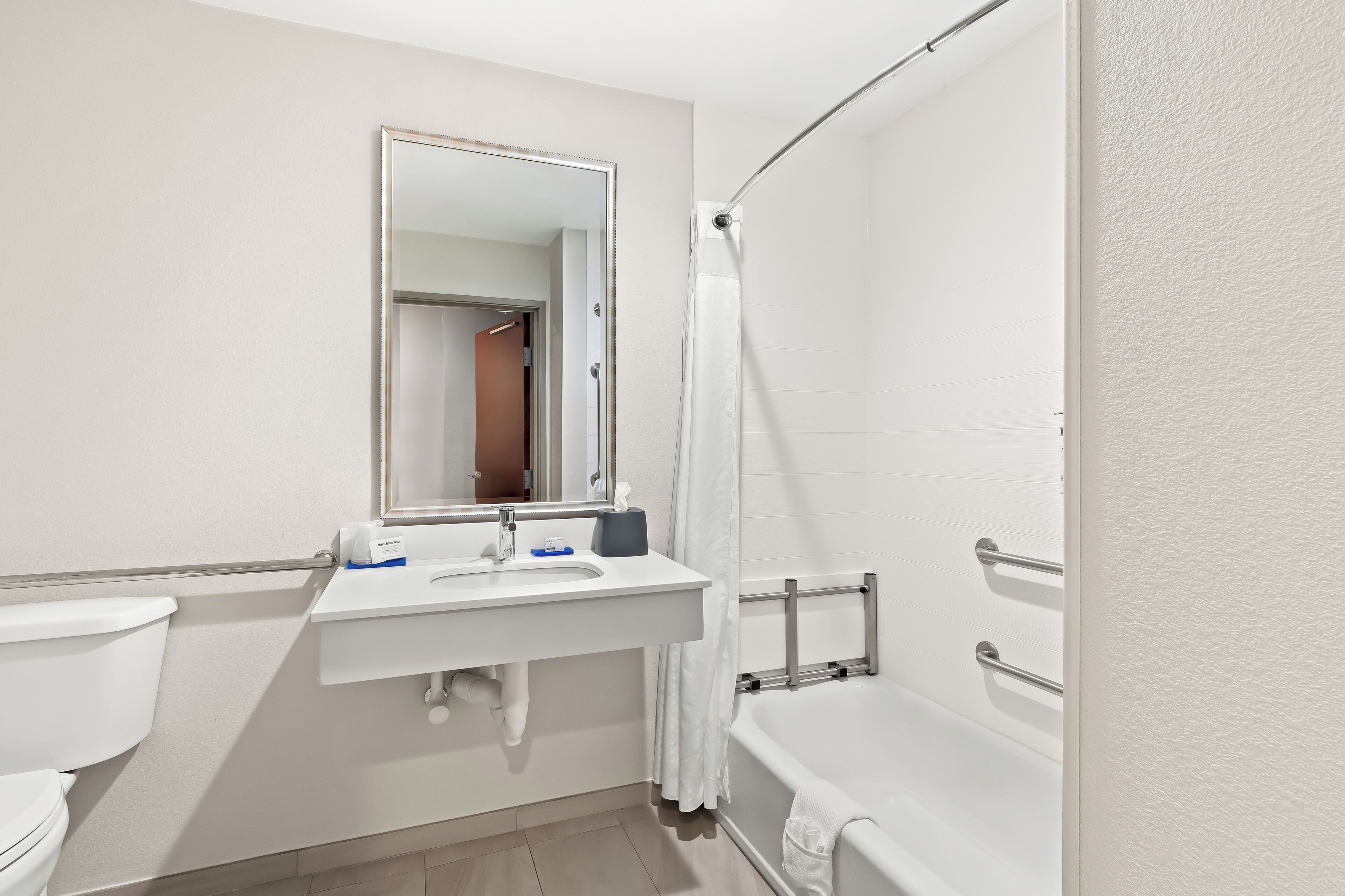 A modern bathroom with a white sink, mirror, toilet, and bathtub.