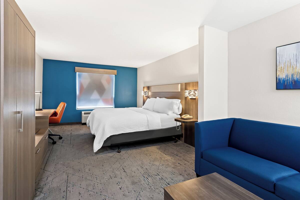 A hotel room with a bed, a desk, a blue sofa, and a painting on the wall.