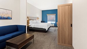 A modern hotel room with a bed, a blue sofa, a wooden coffee table, and a wooden wardrobe. - Holiday Inn Express & Suites Perry by IHG (Perry)