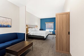 A modern hotel room with a bed, a blue sofa, a wooden coffee table, and a wooden wardrobe.