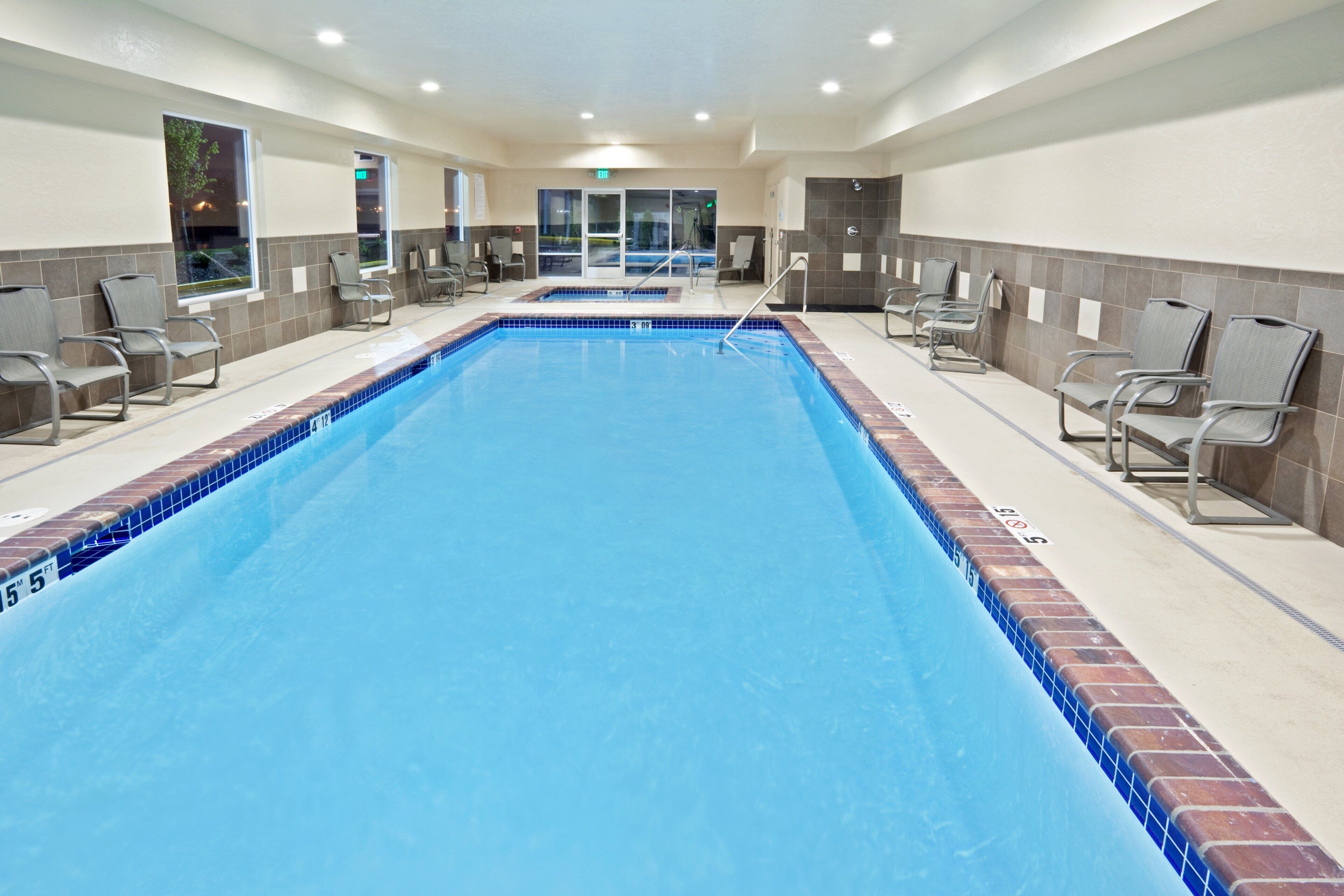A large indoor swimming pool with clear blue water, surrounded by lounge chairs and a tiled wall.