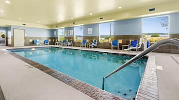 An indoor swimming pool with clear water, surrounded by lounge chairs and a view of the outdoors.