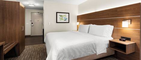 A hotel room with a large bed, wooden headboard, bedside table with a clock, and a framed picture on the wall.
