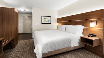 A hotel room with a large bed, wooden headboard, a bedside table with a clock, and a framed picture on the wall.