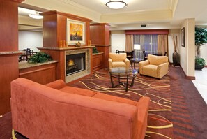 A hotel lobby with a fireplace, seating area, and a dining table.