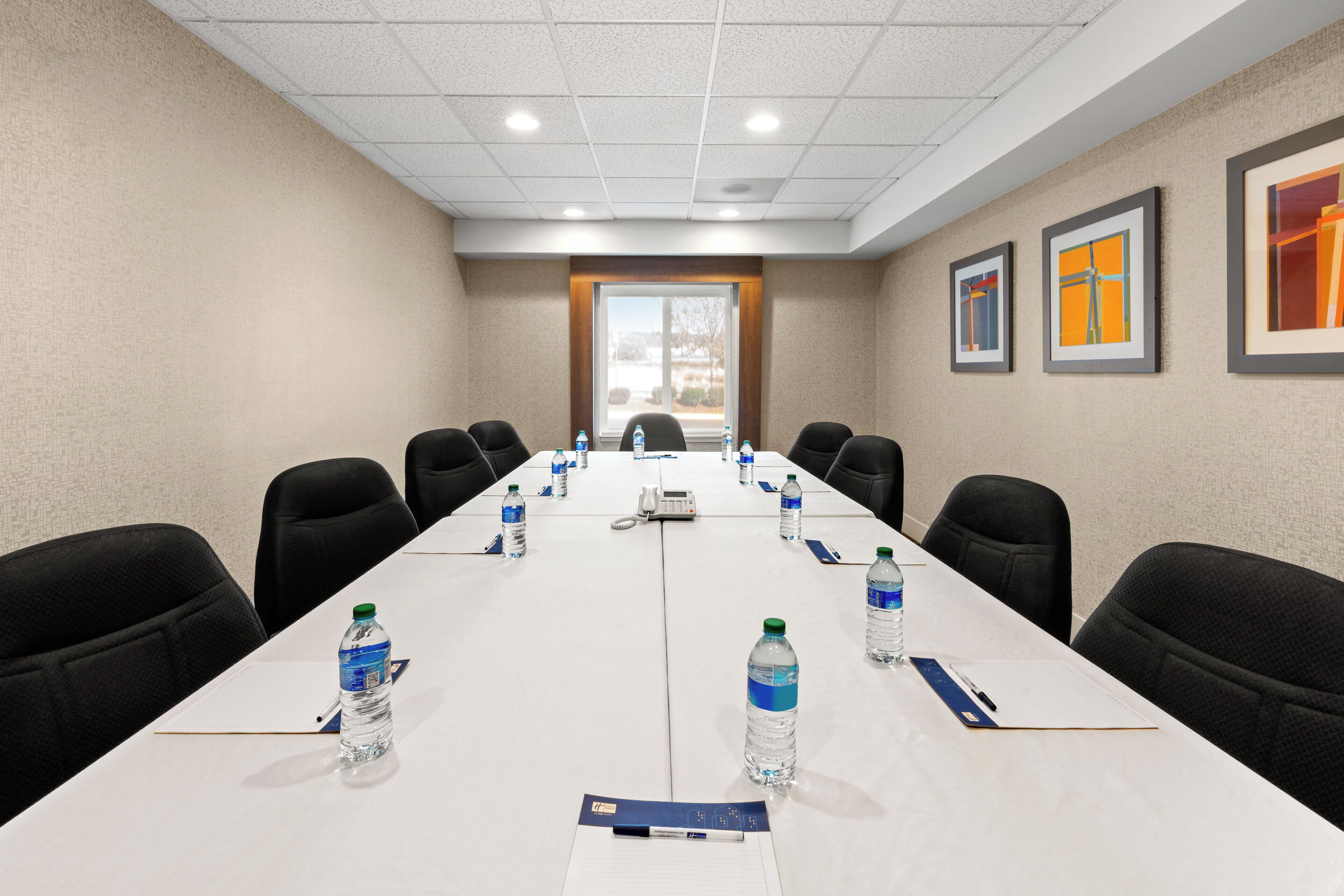 A conference room with a long table, chairs, water bottles, a phone, and framed artwork on the walls.