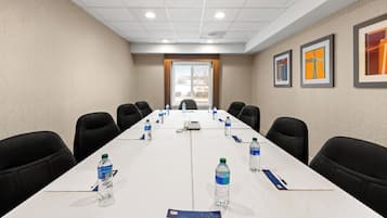 A conference room with a long table, chairs, water bottles, a phone, and framed artwork on the walls.